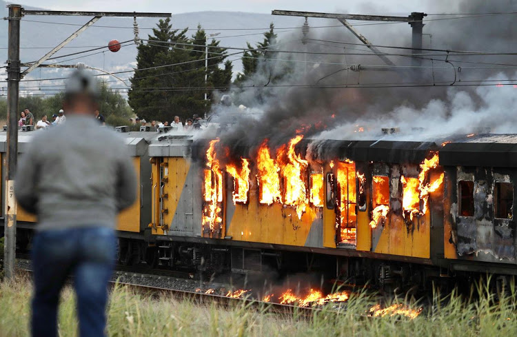 A crowd gathered to watch flames consuming a train between Kentemade and Century City stations, in Cape Town, on January 25 2020.